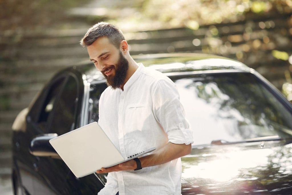 stylish businessman standing near car use laptop