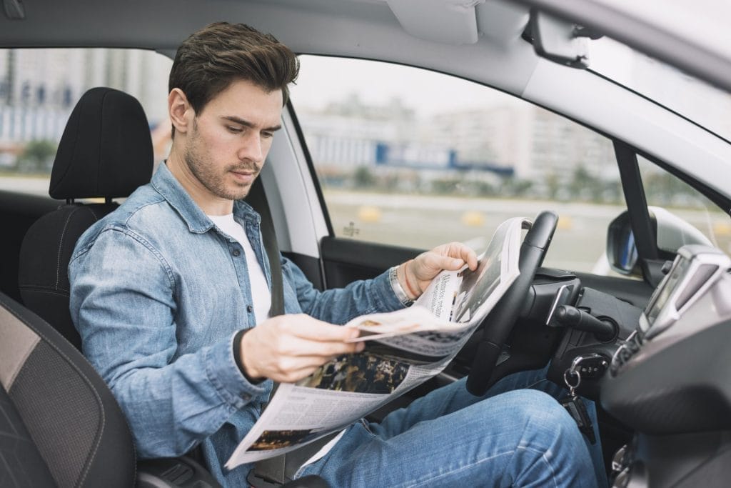 stylish young man sitting luxury car reading newspaper